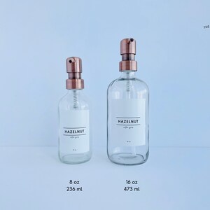May include: Two clear glass bottles with copper-colored pump tops. Each bottle has a white label that reads "HAZELNUT coffee syrup." The smaller bottle is labeled 8 oz (236 ml), and the larger bottle is labeled 16 oz (473 ml).