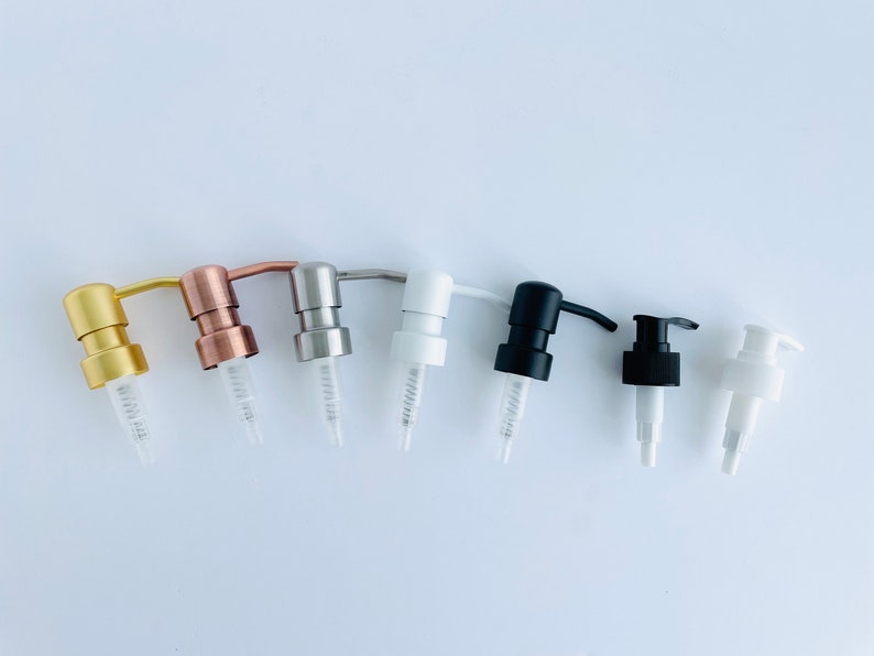 May include: An assortment of soap and lotion dispenser pumps in various colors, including gold, copper, silver, white, and black. Each pump has a clear plastic tube and a curved spout. The pumps are arranged in a row against a white background.