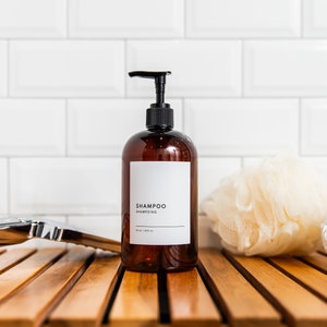 Puede incluir: Una botella de bomba de vidrio ámbar marrón con una bomba negra y una etiqueta blanca que dice "SHAMPOO" sobre una superficie de madera en un baño.