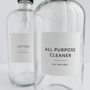 May include: Two clear glass bottles with pump tops and white labels. The label on the left bottle reads "LOTION ALL NATURAL". The label on the right bottle reads "ALL PURPOSE CLEANER ALL NATURAL".