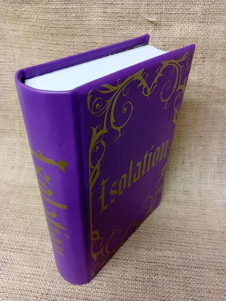 May include: A purple book with the word "Isolation" in gold lettering. The book has gold decorative flourishes around the edges. The pages are white, and the cover is a solid, deep purple.