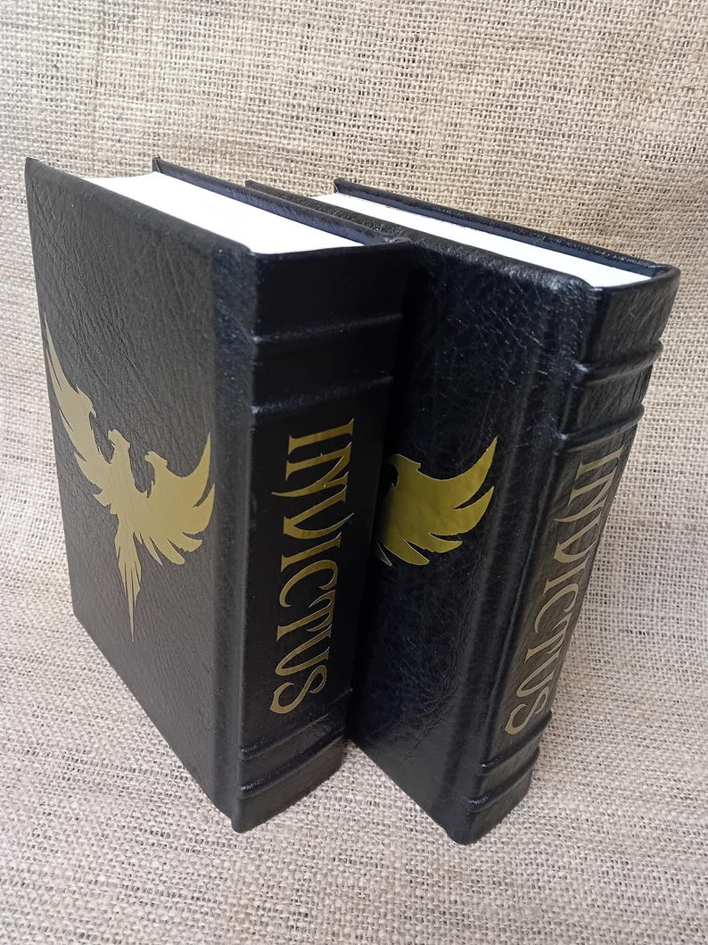 May include: Two black bookends with gold lettering and a gold phoenix design. The word "INVICTUS" is printed vertically on the spine. The bookends have white pages and are made of a textured material.