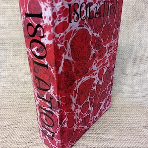 May include: A hardcover book titled "Isolation" with a red and white marbled cover. The title is printed in black on the spine and front cover. The book is standing upright.