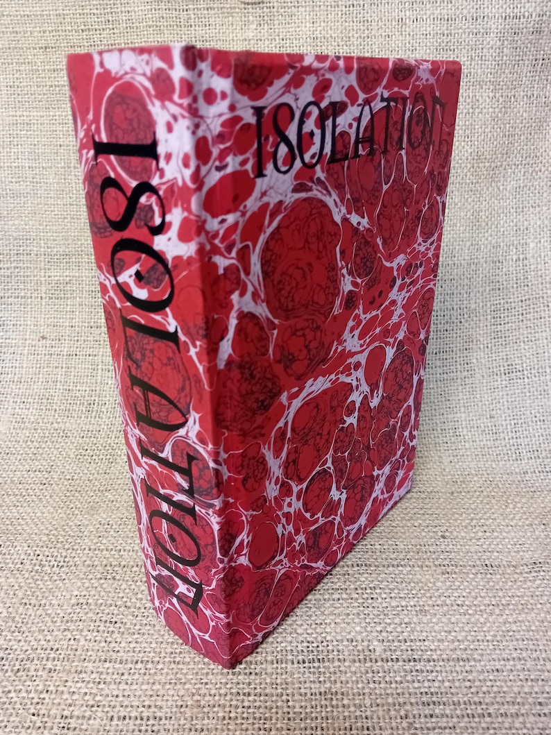 May include: A hardcover book titled "Isolation" with a red and white marbled cover. The title is printed in black on the spine and front cover. The book is standing upright.