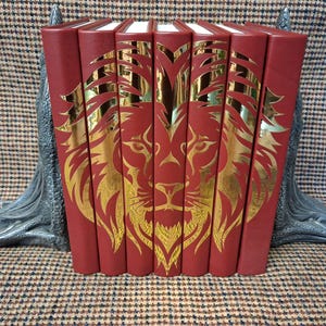 May include: A set of red books with gold lion designs, held by silver dragon bookends. The books are arranged in a row, showcasing the gold lion artwork. The bookends provide support and add a decorative element.