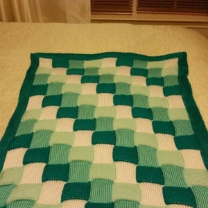 May include: A knitted blanket with a checkered pattern in shades of green and white. The blanket has a green border.