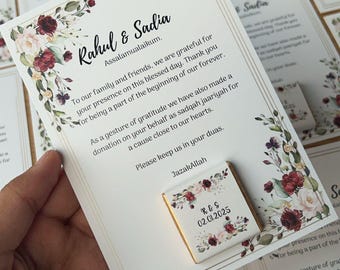 Puede incluir: Una tarjeta blanca con borde dorado y un diseño floral. La tarjeta dice "Rahul & Sadia Assalamualaikum. A nuestra familia y amigos, estamos agradecidos por su presencia en este día bendito. Gracias por ser parte del comienzo de nuestro para siempre. Como muestra de nuestra gratitud, también hemos hecho una donación en su nombre como sadqah jaariyah para una causa cercana a nuestros corazones. Por favor, mantenganos en sus oraciones. JazakAllah" Una pequeña barra de chocolate con un diseño floral y el texto "R & S 02.01.2025" está unida a la tarjeta.