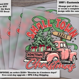 May include: A DTF decal featuring a pink vintage pickup truck carrying pine trees and gift boxes. The text reads SMALL TOWN HOMETOWN Christmas with a wooden sign labeled 38863. A large green bow sits above the truck, all set against a light background.
