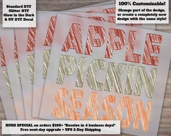 May include: A square DTF decal featuring the text APPLE PICKIN SEASON in a stacked layout. The word APPLE is in red, PICKIN is in a metallic gold, and SEASON is in orange. Each letter has a textured, hand-drawn pencil sketch appearance.