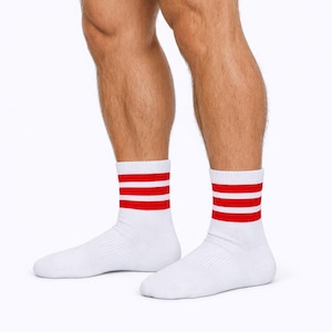 May include: White athletic socks with three red stripes near the top. The socks are ribbed and appear to be made of a soft, breathable material. The socks are worn on a person's feet.