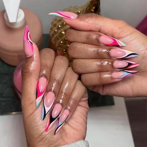 May include: Long, pointed acrylic nails with a pink base and colorful abstract designs. The nails feature a French tip style with black, pink, blue, and white accents. The hands are well-manicured and the nails are glossy.