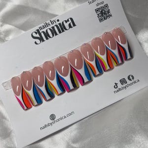 May include: A set of ten artificial nails with a French tip design. The nails have a nude base with a white tip and colorful stripes in orange, yellow, blue, and pink. Each nail is adorned with a small rhinestone. The packaging includes the text "nails by. Shonica".