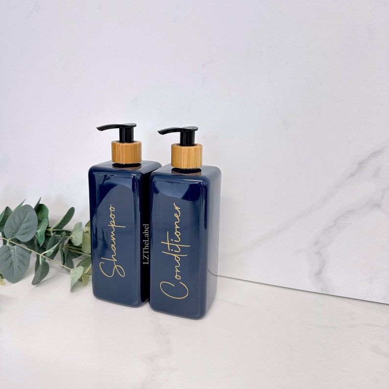 K&ouml;nnte beinhalten: Zwei blaue Pumpflaschen mit Bambusdeckeln und goldener Beschriftung. Die Flasche links tr&auml;gt die Aufschrift "Shampoo" und die Flasche rechts "Conditioner".