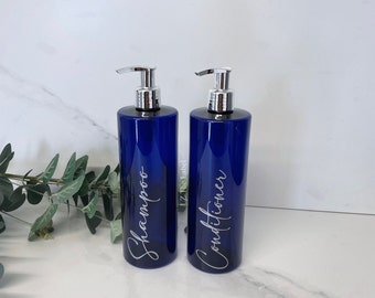 May include: Two blue glass pump bottles with silver tops. The bottles are labeled "Shampoo" and "Conditioner" in a white cursive font.