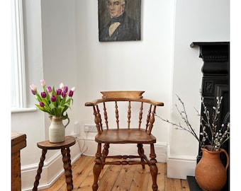 Op de afbeelding: Een vintage interieur met een houten stoel, een kleine bijzettafel en een portret. De stoel heeft een gebogen rug en armleuningen. De bijzettafel heeft een gedraaid pootontwerp. Een terracotta vaas bevat takken.
