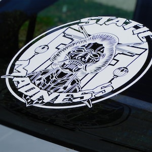May include: A white sticker with a black and white illustration of a skull wearing a samurai helmet and the text "STATE MADNESS" around the outside.