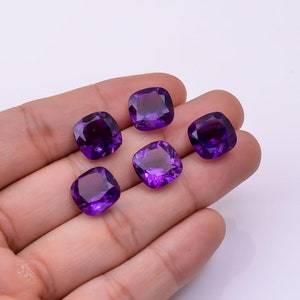 Peut inclure: Six pierres précieuses d'améthyste taillées en coussin, dans différentes nuances de violet, présentées sur une main.