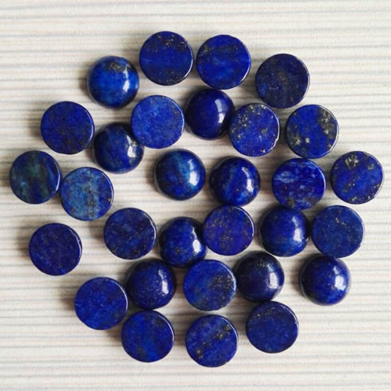 May include: A collection of 25 round, blue lapis lazuli cabochons. The cabochons are smooth and polished, with a deep blue color and flecks of gold pyrite.