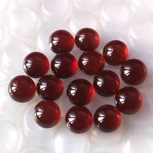 Peut inclure: Un groupe de 16 cabochons ronds en pierres précieuses rouges. Les cabochons sont lisses et polis, avec une finition brillante.