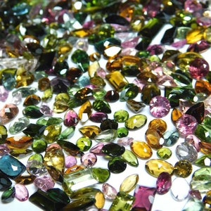 May include: A collection of various green, pink, and brown gemstones. The gemstones are faceted and have a variety of shapes and sizes.