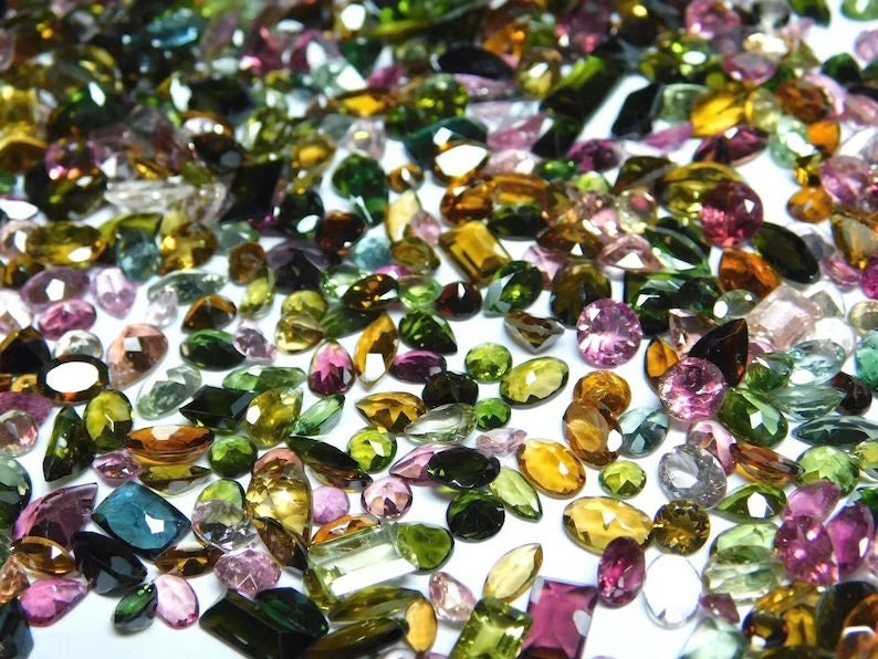 May include: A collection of various green, pink, and brown gemstones. The gemstones are faceted and have a variety of shapes and sizes.