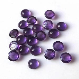 May include: A collection of round, purple amethyst cabochons. The cabochons are smooth and polished, with a slight sheen.