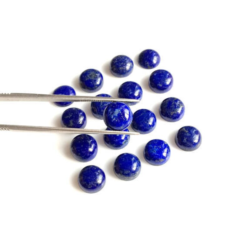 May include: A collection of round, dark blue lapis lazuli cabochons, some of which are being held by tweezers.