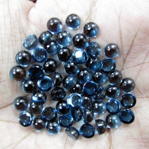Puede incluir: Una colección de cabujones redondos de piedra preciosa azul. Los cabujones son lisos y tienen una forma ligeramente abovedada. Son de color azul oscuro con un ligero brillo.
