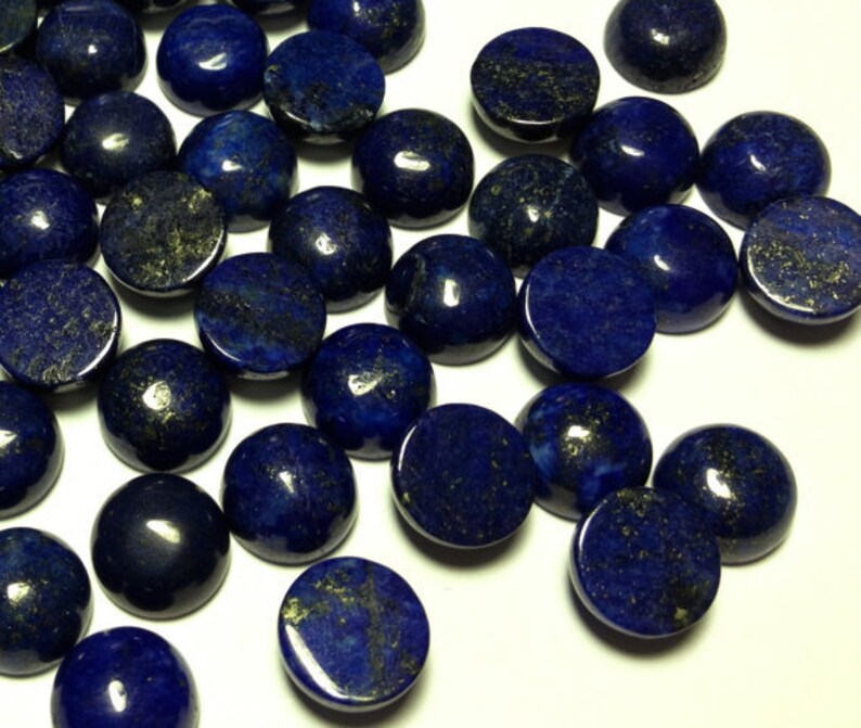 May include: A collection of round, dark blue lapis lazuli cabochons with gold flecks. The cabochons are smooth and polished, and they are arranged in a random pattern.