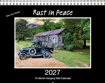 May include: A 2027 12-month hanging wall calendar titled Rust in Peace. The cover features a photograph of a vintage black pickup truck parked on a dirt path in front of a weathered wooden cabin surrounded by green trees and a cloudy sky.
