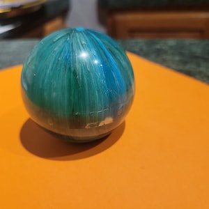 May include: A green and blue sphere with a glossy finish. The sphere has a swirling pattern of light and dark blue and green.