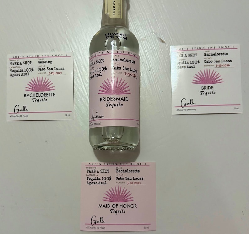 May include: Four small pink and white labels with the text "She's tying the knot!" and "Take a shot Tequila 100% Agave Azul" with a pink sunburst design. The labels are for a wedding, bachelorette party, bridesmaid, and maid of honor. The labels are attached to a clear glass bottle of tequila.