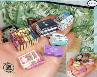 Puede incluir: Una colección de libros en miniatura de varios colores y diseños, incluyendo una pila de libros con un patrón floral, una pila de libros con un diseño en blanco y negro, y una pila de libros con un diseño en verde y blanco. Los libros son todos a escala 1:12.