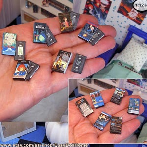 May include: Miniature VHS tapes and movie covers are held in a hand. The tapes and covers feature colorful anime-style artwork. The collection includes titles like "My Neighbor Totoro" and other animated films. The scale is 1:12.