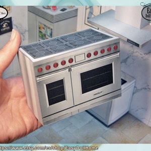 May include: A silver double oven with a black glass top and red knobs. The oven has a "WOLF" logo on the front. The oven is 1:12 scale.