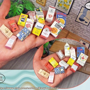 Könnte beinhalten: Eine Sammlung von Miniatur-Lebensmittelverpackungen, darunter Kaffee, Zucker und Müsli. Die Artikel sind in verschiedenen Farben und Designs gehalten und mit Text beschriftet. Der Maßstab ist 1:12.