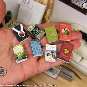 Może przedstawiać: Kolekcja miniaturowych książek, w tym Duma i uprzedzenie, Jane Eyre,  Księżniczka Panna Młoda i Rozważna i romantyczna. Książki są ułożone na dłoni, z etykietą skali 1:12 w prawym górnym rogu.