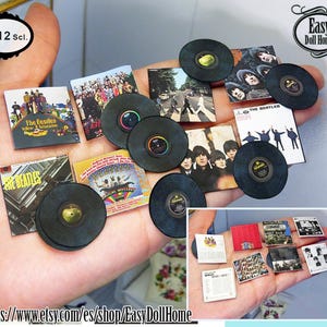 Puede incluir: Una colección de portadas de álbumes y discos de vinilo en miniatura de los Beatles, incluyendo "The Beatles", "Sgt. Pepper's Lonely Hearts Club Band", "Abbey Road" y "The Beatles (White Album)". Los discos son a escala 1:12 y se muestran en una mano.