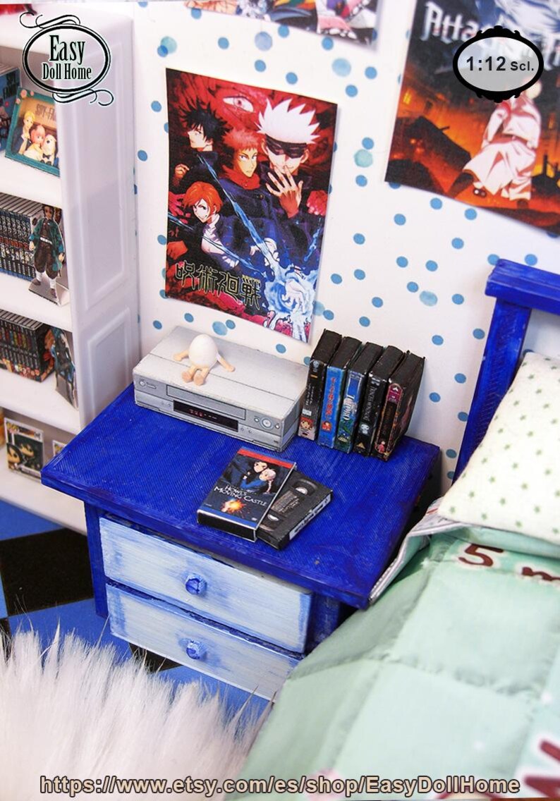 May include: Miniature bedroom scene with a blue nightstand, a VCR, and several VHS tapes. A poster with Japanese text hangs on the wall. The scene includes a bed with a green and white patterned comforter. The scale is 1:12.