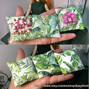 Op de afbeelding: Vijf miniatuur kussens met tropische blad- en bloemenpatronen. De kussens zijn wit met groene bladeren en roze en rode bloemen.