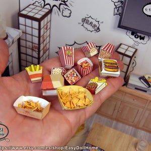 Op de afbeelding: Miniatuur fastfood-items, waaronder popcorn, friet, een hamburger en nacho's, worden in een hand gehouden. De items zitten in kleine, gedetailleerde papieren bakjes. De achtergrond omvat een miniatuur-tv en een kast.