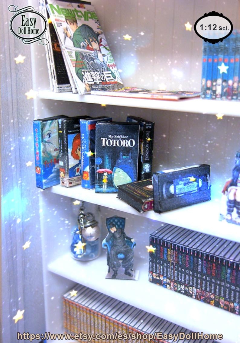 May include: Miniature white bookshelf with various items. Includes magazines, VHS tapes, and books, including "My Neighbor Totoro." The shelf also features small figurines and a collection of miniature books. The scale is 1:12.