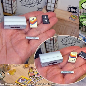 May include: Miniature silver VCR with a remote, a VHS tape labelled E-180, and a black VHS tape. These dollhouse accessories are held in a hand, with a comic book background.