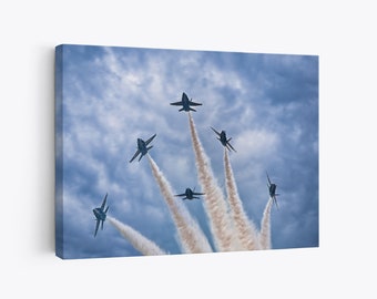 May include: Six blue and white fighter jets fly in formation, leaving white smoke trails against a cloudy blue sky.