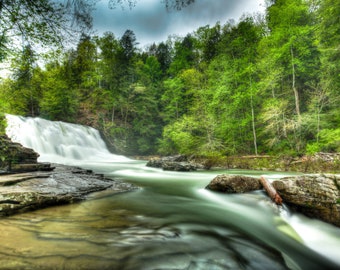 Könnte beinhalten: Ein Wasserfall stürzt durch einen üppigen grünen Wald. Das Wasser ist klar und die Felsen sind mit Moos bedeckt. Die Bäume sind hoch und die Blätter sind leuchtend grün.