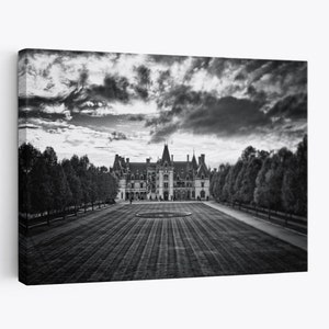 May include: A black and white photograph of a large, grand house with a long driveway leading up to it. The house has a symmetrical design with multiple towers and a large lawn in front of it. The sky is cloudy and dramatic.