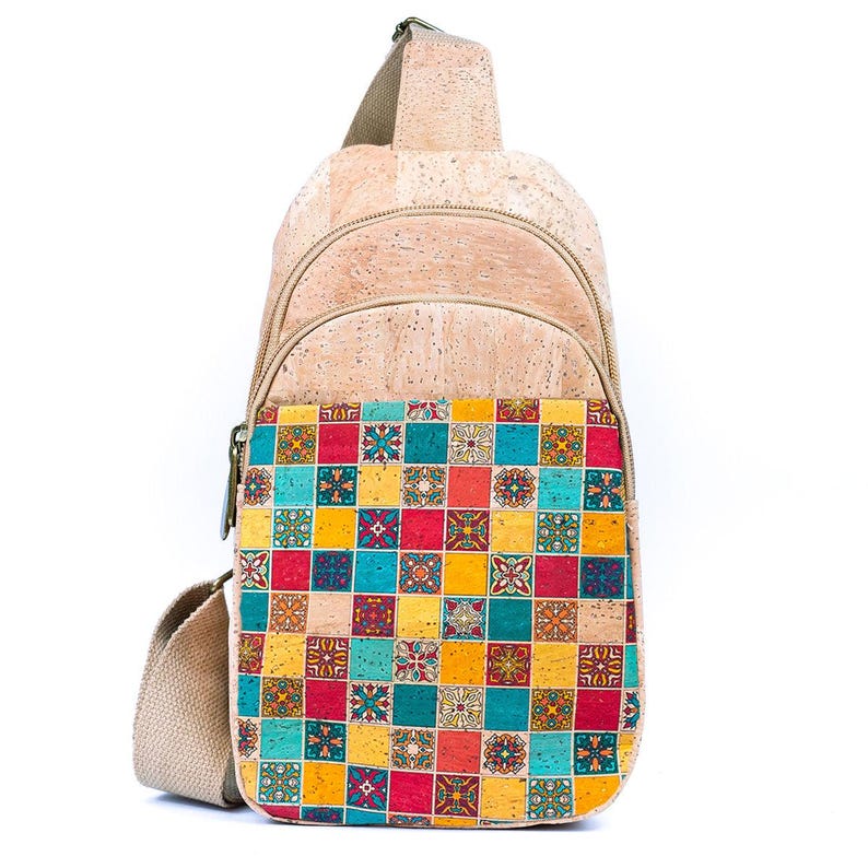 May include: A sling backpack crafted from natural tan cork material. The front pocket features a vibrant, multi-colored grid pattern of squares in teal, yellow, and red, with some squares containing intricate floral-inspired geometric designs.