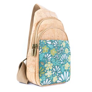 May include: A tan cork sling backpack featuring a front pocket with a teal, green, and white floral pattern. The bag includes two zippered compartments with metal pulls stamped with the word Portugal and a wide, adjustable beige fabric shoulder strap.