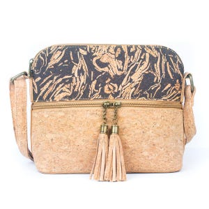 May include: A crossbody bag made of cork material. The top section features a dark pattern, while the bottom is a lighter cork color. The bag has a zipper closure with two tassel accents and an adjustable strap.