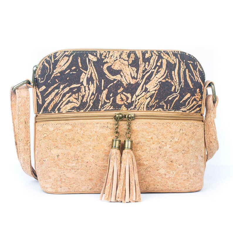 May include: A crossbody bag made of cork material. The top section features a dark pattern, while the bottom is a lighter cork color. The bag has a zipper closure with two tassel accents and an adjustable strap.